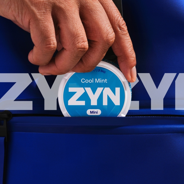 Main glissant une boîte de sachets de nicotine ZYN bleue dans une poche