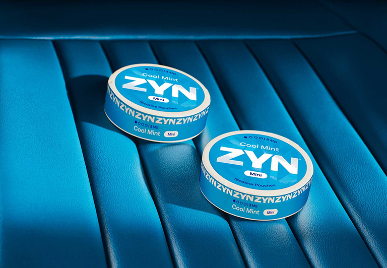 Two closed blue ZYN Cool Mint cans Mini on a soft blue shelf
