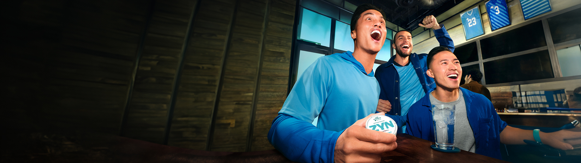 People watching a game on TV; one of them is holding a ZYN nicotine pouch can