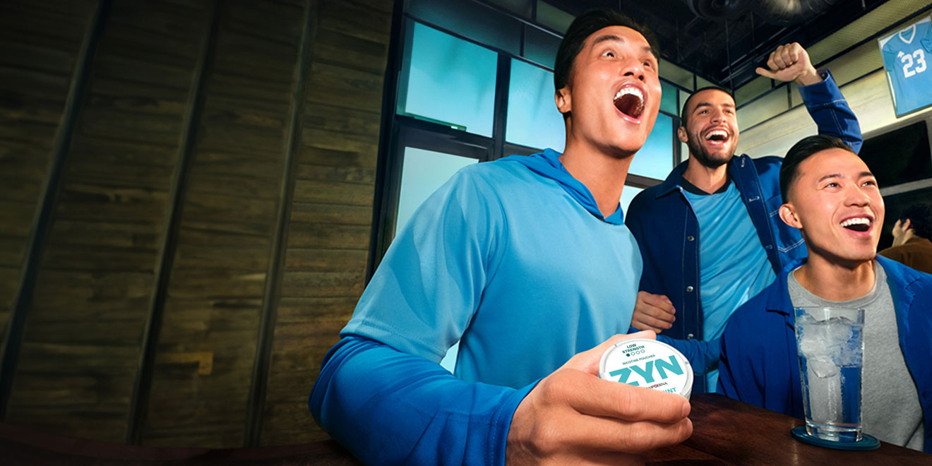 People watching a game on TV; one of them is holding a ZYN nicotine pouch can