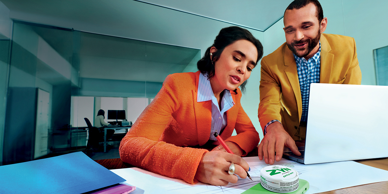 Man and woman talking in the office; a ZYN nicotine pouch can on the table