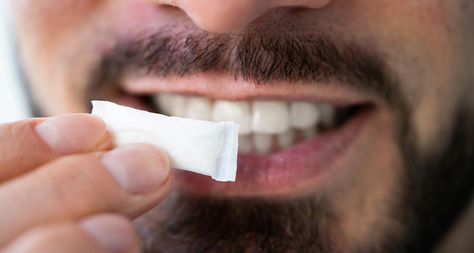 Nahaufnahme einer Hand, die einen weißen Nicotine Pouch vor dem Mund hält.