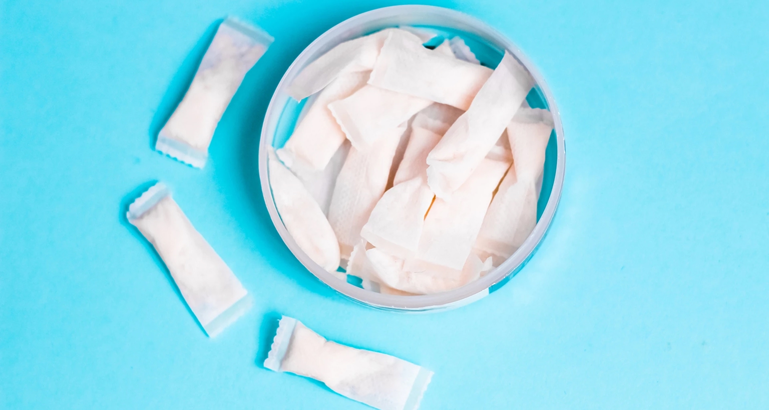 Offene Dose mit weißen Nicotine Pouches auf blauem Hintergrund, einige Pouches liegen neben der Dose.