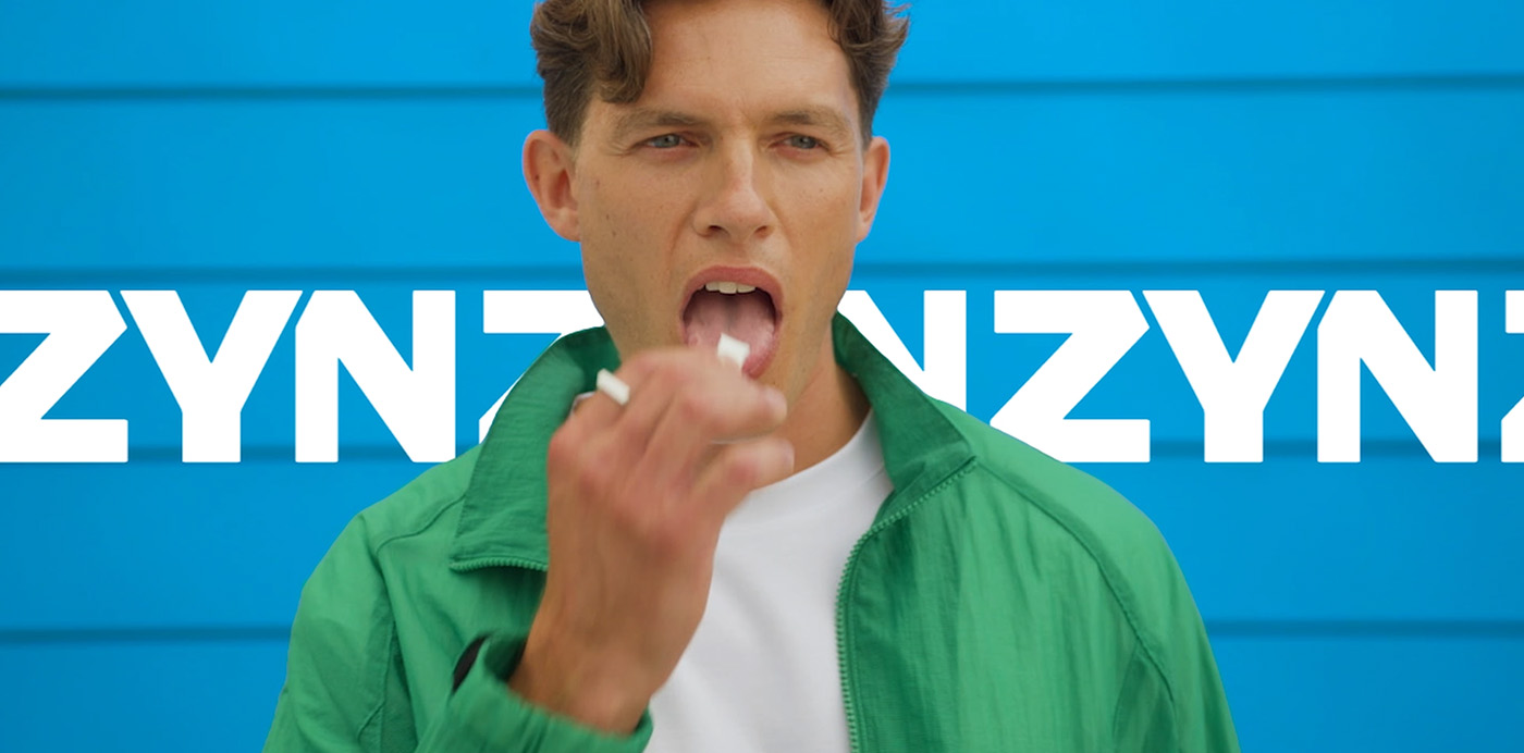 Découvre Zyn -  un homme portant une chemise blanche et un sweat vert devant un logo ZYN