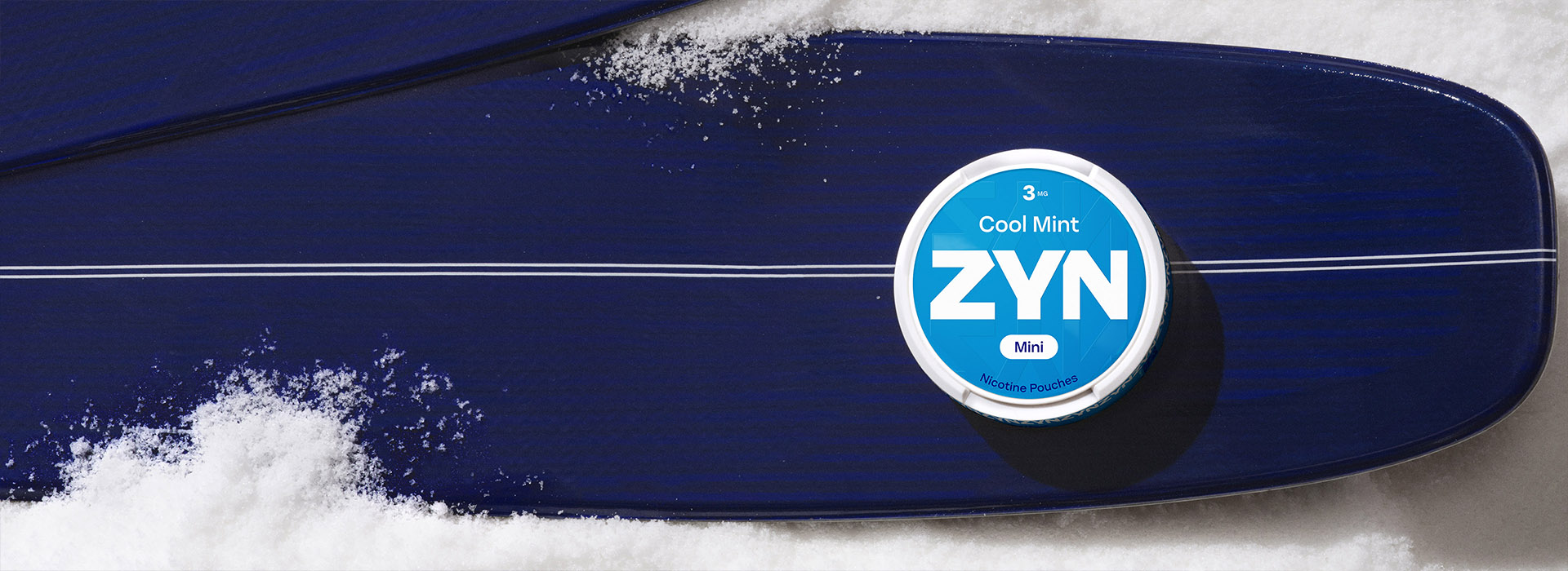 une boîte de sachets de nicotine ZYN Cool Mint bleue 3 mg Mini posée sur un ski dans la neige