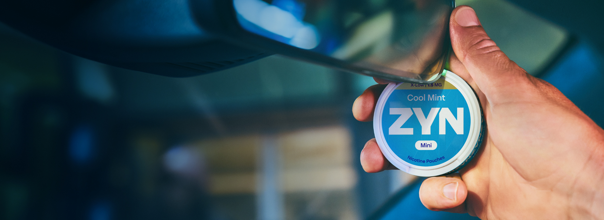 Hand holding a can of ZYN nicotine pouches inside a car.
