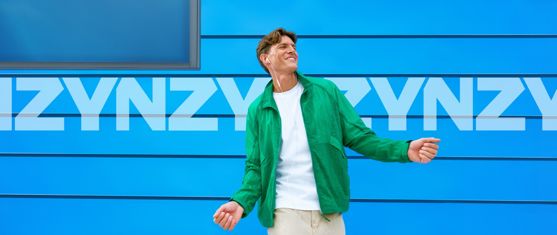 Hombre vestido con camisa blanca y sudadera verde, escuchando música.