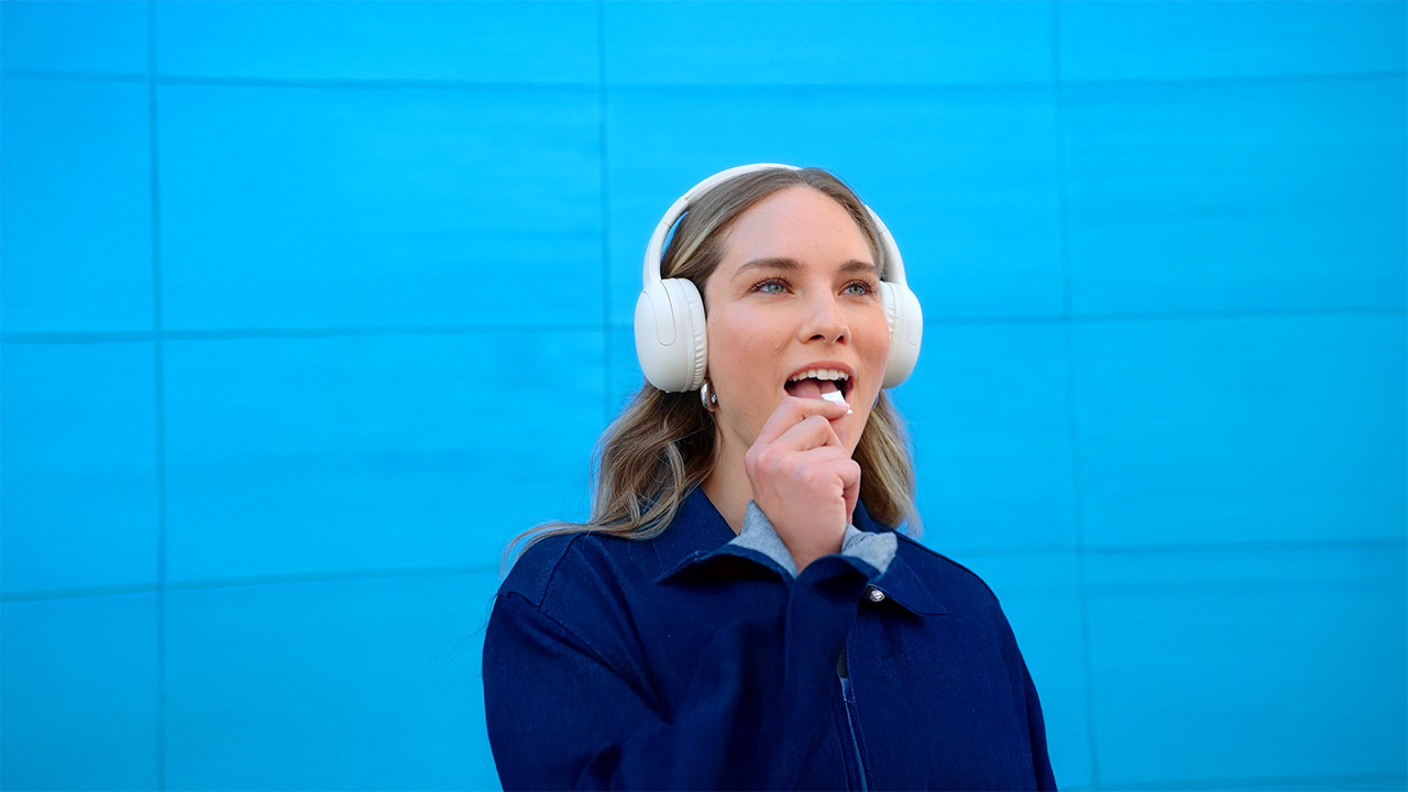 Mujer con suéter azul, escuchando música mientras prueba una bolsita de nicotina ZYN