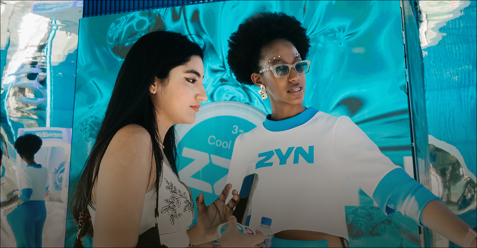 Dos personas frente a una instalación color turquesa con branding de ZYN en un festival