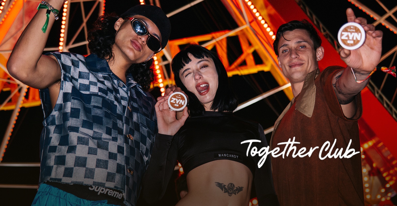 Grupo de personas en un festival nocturno levantando latas de ZYN, con luces de juegos mecánicos.