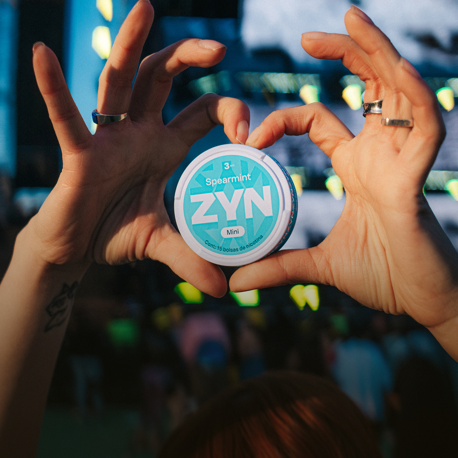 Primer plano de una mano sosteniendo una lata de ZYN, con iluminación natural y ambiente de festival