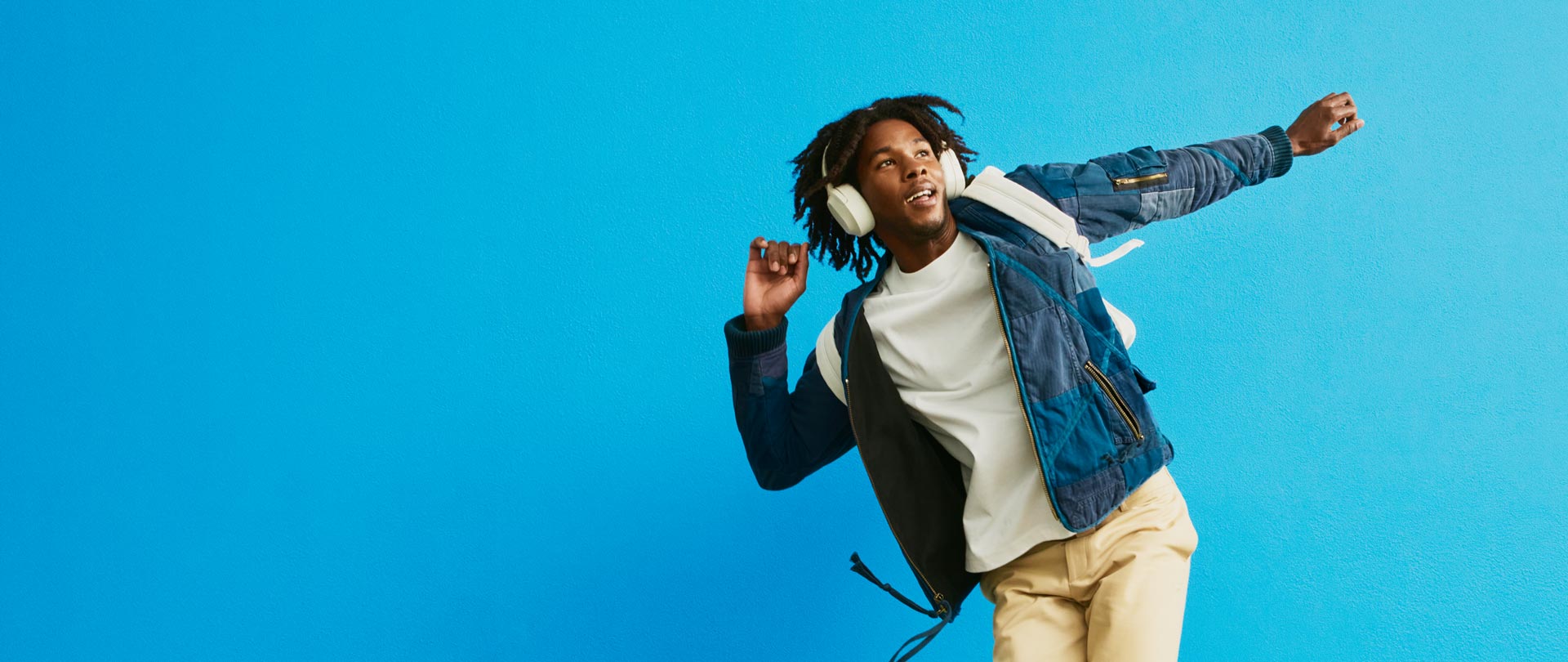 Hombre con playera blanca sonriendo y extendiendo la mano - pared azul al fondo - ZYN