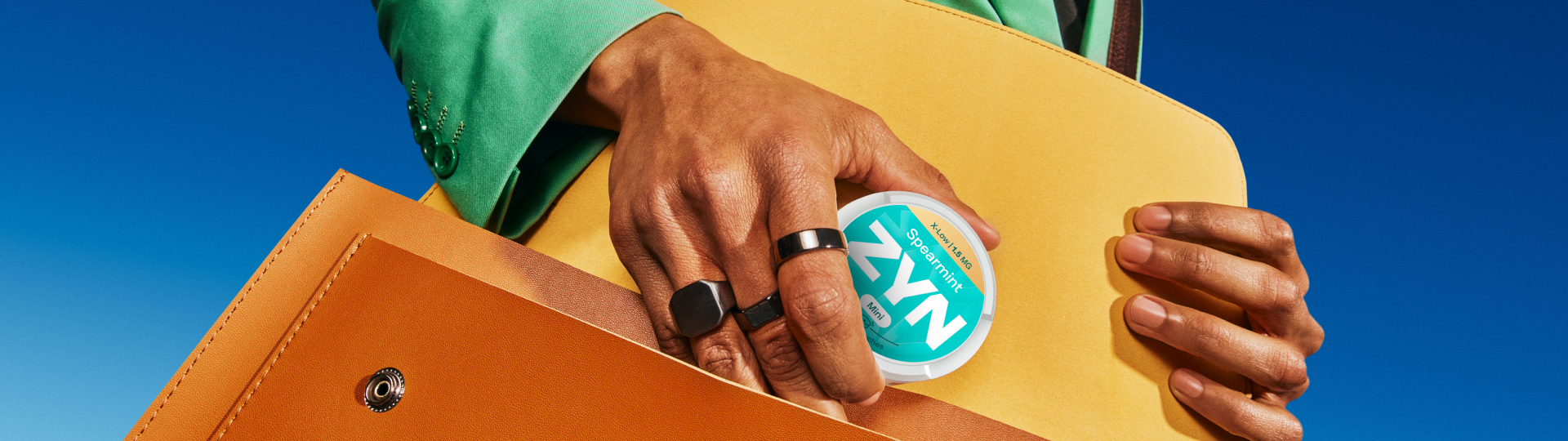 Detailný záber ruky ozdobenej rôznymi prsteňmi, ktorá drží škatuľku ZYN Spearmint X-Low.