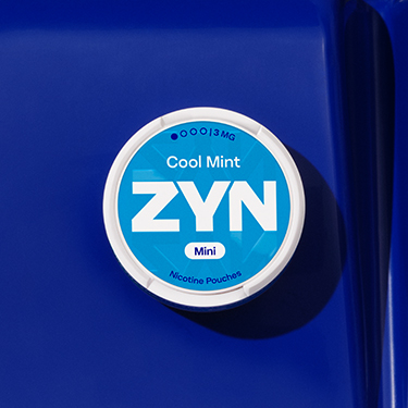 Niebieskie opakowanie saszetek nikotynowych ZYN Cool Mint leżące na granatowym plastikowym siedzisku