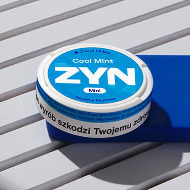 Niebieskie opakowanie saszetek ZYN leżące na grantowym etui telefonu na szarym stoliku