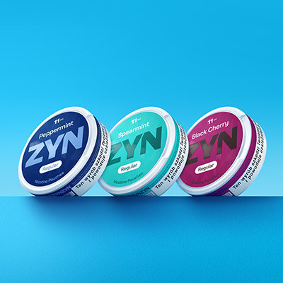 Puszki ZYN na niebiskim tle. ZYN Pepperminty 11 mg w kolorze granatowym, ZYN Spearmint 11 mg w kolorze jasnozielonym, ZYN Black Cherry 11 mg w kolorze bordowym